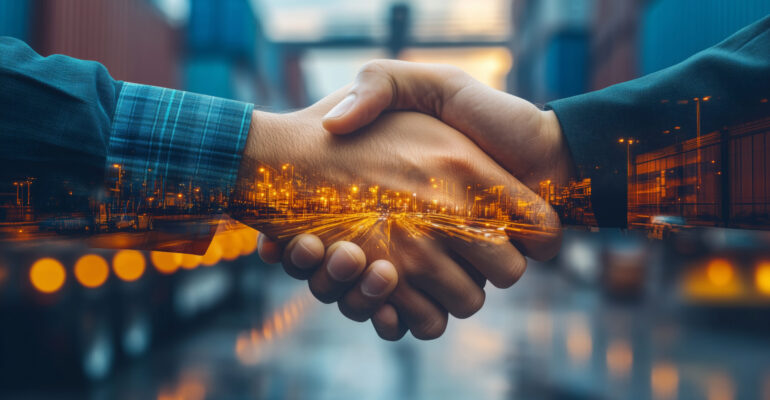 Handshaking between business partners amid bustling international logistics transportation hub at twilight