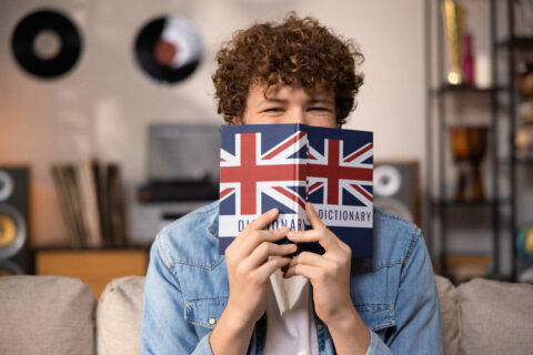 A teenager with curly hair sits focused in a room studying for an English exam. A boy in a blue jean shirt prepares for an English job interview