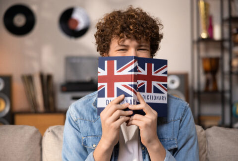 A teenager with curly hair sits focused in a room studying for an English exam. A boy in a blue jean shirt prepares for an English job interview