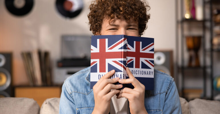 A teenager with curly hair sits focused in a room studying for an English exam. A boy in a blue jean shirt prepares for an English job interview